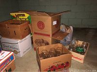Boxes filled with glass mason jars and large glass jars stored in cardboard boxes in a basement or storage area.
