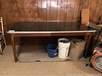 Front view of table showing black Formica top, solid wood legs, and base with some items underneath.