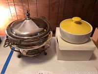 Photo showing metal warming server with lid and Pyrex bowl inside next to yellow casserole dish on original box
