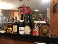 Photo of decorative wine bottles including Amaro and sparkling wines, vintage globe bookends with map design and Black Label bar light on top of a bar counter.