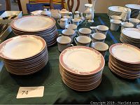 Wide view of all china pieces including stacks of bowls, plates, saucers, and cups arranged on table showing overall quantity and consistent Taupe Fantasy pattern.