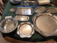 Photo showing all silver plate trays and glass serving bowl on table, displaying varying shapes and sizes from small to large.