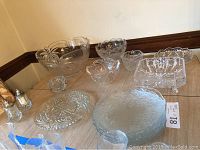 Overview of various crystal bowls, plates, square pedestal dish, and salt and pepper shakers on a wooden surface.