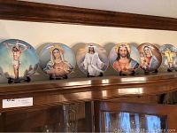 Six Franklin Mint religious collectible plates displayed on a wooden cabinet top, each on a stand.