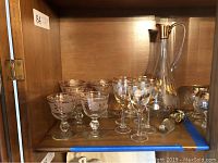 Photo showing the decanter and matching glasses arranged inside a cabinet shelf under warm lighting.