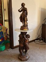 Full view of the bronze flute player statue on marble cherub pedestal table in a room corner