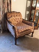 Front and right side view of vintage carved wood armchair with floral patterned upholstery and tufted backrest.