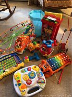 Wide view showing entire collection of toddler toys including musical instruments, building sets, and toy cars arranged on floor near furniture.