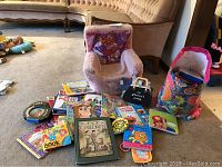 Photo of the toddler chair, assortment of children's books and VHS tapes spread out on carpeted floor near a couch and toys.