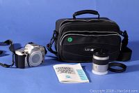 Photo of camera body, zoom lens, manual, and Minolta branded carrying case arranged on blue background.