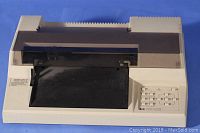 Front view of beige Hewlett Packard plotter with transparent plastic cover and input/output trays visible.