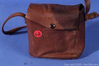 Brown leather camera case with a snap button closure and thin adjustable strap, showing signs of wear and use.
