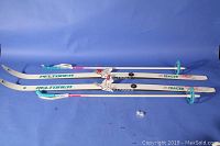 Pair of Peltonen junior cross country skis with bindings, white with teal and purple graphics, laid flat to show overall condition and length.