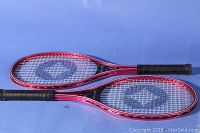 Pair of red and black metal tennis rackets with Spalding logo on strings, lying parallel on blue background.