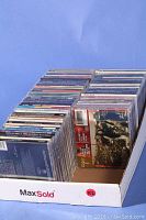 Box containing about 72 popular music CDs, arranged side by side, showing spines with album and artist names, mostly intact jewel cases.