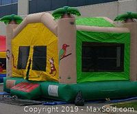 Inflated bounce house with beige, green and yellow vinyl, palm tree columns, parrot and monkey graphics, mesh windows.