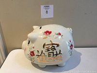 Side view of the large white ceramic piggy bank showing gold Asian characters and floral accents