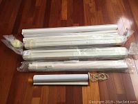 Seven window coverings including a Hunter Douglas roller blind wrapped in plastic, laid out on floor showing lengths and wrapped conditions.