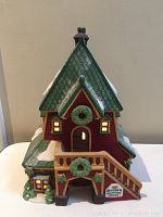 Front view of Department 56 North Pole Series Santa's Rooming House ceramic building with green roof, red walls, snow decorating, wreaths, a small staircase, and a sign.