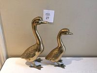 Front view of two brass duck sculptures showing sizes and detailed feathers.