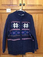 Front view of navy blue cardigan sweater with white and pink snowflake and diamond patterns hung on hanger.