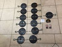 Ten 6-inch cast iron wood stove dampers laid out on tile floor, showing black and some rusty surfaces, all with long metal handles.