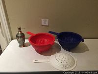 Tupperware colanders in red and blue with white lid in front and silver soap dispenser pump on the left.
