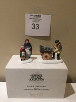 Front view of both handpainted porcelain figurines displayed on their original box, showing the woman with child and the man with knife grinder cart on snow bases.