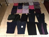 Full lot of 24 pieces of mostly size XL ladies clothing including tops and bottoms in multiple colors and fabrics, laid out on the floor.