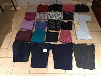 Full view of 22 folded ladies clothing items laid out on floor showing various tops, jeans and pants in different colors and patterns.