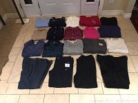 Lot of 19 used ladies clothing items including tops, sweaters, pants in various colors and fabrics laid out neatly on a tiled floor.