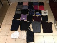Photo of 27 women's clothing pieces spread out on floor, showing mix of tops, pants, skirts, and dresses in various colors and prints.