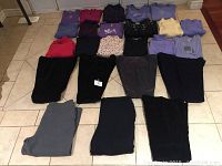 24 pieces of ladies clothing from Northern Reflections spread out on tiled floor, including tops, sweaters, and pants in various colors and patterns