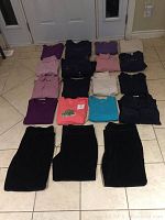 Photo of folded ladies clothing items laid out on tile floor showing a variety of tops and skirts in colors including purple, pink, black and beige.