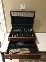 Wooden chest open showing green fabric-lined slots with assorted flatware pieces and knife drawer below.