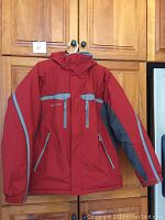 Columbia men's winter coat with hood hanging on a cabinet, showing full front side with red and gray colors and multiple zippered pockets