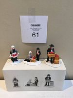 Photo of all three Amish family porcelain figurines displayed on and in front of original box, showing details of each figure and the white bases.