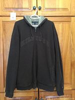 Front view of brown Tommy Hilfiger men's hoodie, full zip, with hood visible. Hoodie appears in good used condition with 'HILFIGER' embossed across chest.
