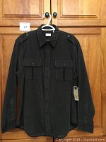 Full view of men's grey corduroy shirt with buttoned chest pockets and shoulder epaulets, hanging on a hanger.