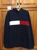 Front view of the navy blue hoodie with a horizontal white and red stripe across the chest, featuring a kangaroo pocket and hood.