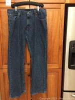 Front view of dark blue denim Tommy Hilfiger Freedom Fit men's jeans hanging on a black hanger, showing full length, classic five-pocket design.