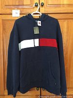 Front view of navy Tommy Hilfiger hooded sweatshirt with white and red stripe, hanging on a hanger
