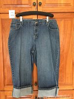 Front view of blue denim capri pants hanging on black hanger against wood door.
