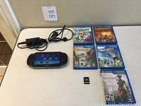 Overall lot view: console, charger, six game cases, game card and memory card on table