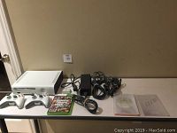 Xbox 360 console with controllers, power adapter, cables, and game on a table