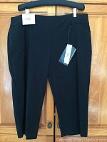 Full view of black capri pants displaying elastic waistband and new tags.