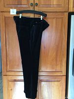 Side view of navy blue DG2 Diane Gilman women's pants hanging on a black hanger against wooden cabinet.