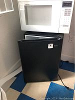 Haier black mini fridge with Electrolux microwave on top, closed view