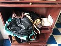 Wood shelving unit containing multiple purses and wallets, including a prominent black leather bag and smaller handbags in brown and white.