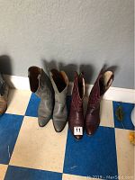 Two pairs of men's cowboy boots, gray pair and dark red pair, size 9.5, positioned side by side against a wall on a blue and white checkered floor.